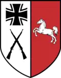 Wappen in Schildform. In der rechten Hälfte auf Silber das Eiserne Kreuz in Schwarz und Silber, darunter zwei gekreuzte Karabiner in Schwarz. In der linken Hälfte das weiße Niedersachsenross auf Rot.