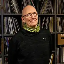 Helmut Philips steht vor einem Plattenregal und schaut reserviert in die Kamera