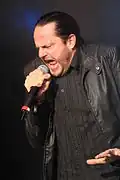 Henke singend mit Mikrofon und gebundenen schwarzen Haaren