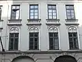 Im Mittelteil sind die Flächen zwischen den vier Fenstern des ersten und zweiten Obergeschosses mit Bögen, weiblichen Kopfmasken und Tüchern aus dem Stuckformenrepertoire des Empire (Stilrichtung) dekoriert.