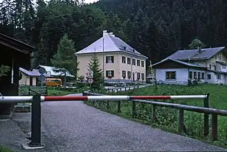 Blick vom deutschen zum österreichischen Staatsgebiet (1980). Rechts: Alpengasthof, Mitte: ehemaliges österreichisches Zollhaus (heute: Herberge Bergheim), links (Anschnitt an dem Schlagbaum): deutsche Grenzerhütte.