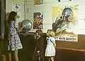 Klassenraum. Hintergrund: Plakate zur Zeichnung von Kriegsanleihen