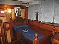 Kajüte des Kapitäns mit Bild von Miguel Grau. Das runde Gerät an der Decke ist keine Lampe, sondern der von Grau angebrachte, vom Bett aus ablesbare Kompass.