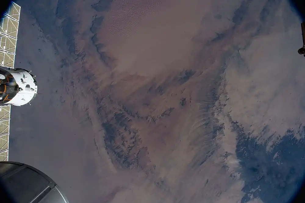 Bild von der Internationalen Raumstation aus mit den dunklen Tibesti-Gebirgszügen im Osten (rechts unten) und der orangefarbigen Murzuk-Sandwüste im Norden (oben).