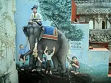 An einer Mauer (vielleicht in einem Tempel) ist das Gleichnis der Blinden mit dem Elefanten als Relief abgebildet. Die Darstellung könnte etwa einen Meter hoch sein; sie ist naturnah und sehr plastisch ausgeführt und in natürlichen Farben koloriert. Die Gruppe steht auf einer Anhöhe, hinter der sich eine weite, nur angedeutete Landschaft bis zum Horizont erstreckt. Der Himmel ist hellblau. Unmittelbar hinter dem Elefanten steht ein großer, sehr detailreich dargestellter Baum, rechts daneben befindet sich eine Tafel mit thailändischen Schriftzeichen. Der dunkelgraue Elefant steht mit dem Kopf nach links quer vor uns. Er hat den Kopf dem Betrachter zugewandt und scheint sich an dem Tun der Männer nicht zu stören. Über seinen Rücken ist eine Decke geworfen, sie zeigt ein blaues Rautenmuster und hat eine gelbbraune Bordüre. In seinem Nacken hockt im Schneidersitz ein Elefantenführer in schmucker Uniform mit dunkler Hose und weißem Hemd, er hat einen gezwirbelten Schnurrbart und trägt einen mit einer weißen Feder geschmückten blauen Hut. Er scheint nicht zu den Blinden zu gehören. Sechs blinde Männer stehen oder hocken um den Elefanten herum. Sie sind mit einfachen Hemden und Hosen bekleidet und barfuß. Sie betasten mit geschlossenen Augen ein Ohr, den Rüssel, einen Stoßzahn, einen Oberschenkel, den Bauch und den Schwanz des Tieres, welches dies ungerührt über sich ergehen lässt.