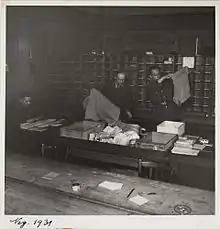 Innenansicht Büroraum Interniertenpost Schweiz, Abbildung ca. von 1939 bis 1945, Bild zeigt Personen beim Leeren der Postsäcke und beim Sortieren der Post, im Hintergrund ist ein Sortiergestell sichtbar.