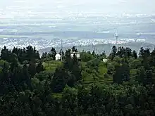 Blick vom Aussichtsturm des Großen Feldbergs zum Gipfel des Kleinen Feldbergs, dahinter der Fernmeldeturm auf dem Atzelberg und der Ort Bremthal sowie am Horizont Wiesbaden