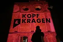 Der Schrifszug Kopf & Kragen Literaturverlag wird mit einem Lichtprojektor auf die Hauptfassade der Ruine des Anhalter Bahnhofs in Berlin geworfen.