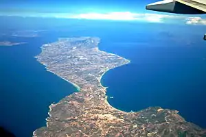 Luftaufnahme der Insel, Blickrichtung von der Kefalos-Halbinsel noch Kos Stadt. Vorne links die Bucht von Kochylari, gegenüber ein Teil des Golfs von Kefalos. Deutlich erkennbar der „Hals“, den beide Buchten bilden und wodurch die Kefalos-Halbinsel von der restlichen Insel Kos deutlich abgeteilt wird. Rechts hinten ist das Gebirge Dikeos gut zu sehen, ganz im Hintergrund die türkische Küste (Festland).