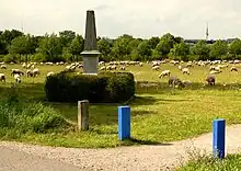 Der „Paradestein“ zur Erinnerung an die Kaisermanöver am Kronsberg, hier mit blauen Wegmarkierungen des Grünen Rings