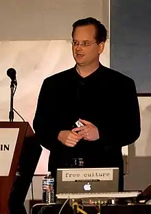 Lawrence Lessig stehend auf einem Podium mit Mikrofon, mit einem Laptop vor ihm.