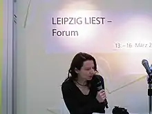 Martina Weber spricht in ein Mikrofon, über ihr ein Schriftzug "LEIPZIG LIEST - Forum"