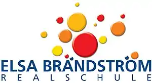 Das Logo der Schule zeigt rote, gelbe und orangefarbene Kreise unterschiedlicher Größe, darunter den Namen der Schule
