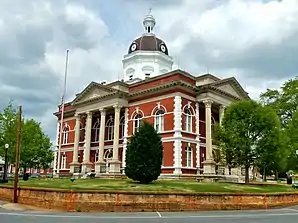 Meriwether County Courthouse (2013). Das Courthouse entstand 1903/04 im Stil der Colonial-Revival-Architektur und ersetzte einen Vorgängerbau von 1832. Ausführender Architekt war J. W. Golucke, auf den viele Gerichts- und Verwaltungsgebäude in Georgia  und Alabama zurückgehen. Im Mai 1973 wurde das Meriwether County Courthouse als zweites Objekt im County in das NRHP eingetragen.