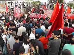 Kundgebungsteilnehmer mit rot eingeschlagenen Särgen, roten Fahnen und Bildern der Opfer