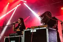 Beide Frauen sind auf der in rotes Licht getauchten Bühne zu sehen Hélène de Thoury‎ steht am Synthesizer mit wehenden Haaren. Die hinter einem Synthesizer stehende Amandine Stioui hält sich das Mikrophon vor den Mund und singt.