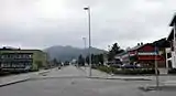 Foto einer Straße, links und rechts davon Gebäude, im Hintergrund Berge