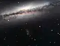 Aufnahme mithilfe des Very Large Telescope. Unter­halb der Bild­mitte is eine diffuse Satelliten­galaxie als bläu­liche Wolke zu erkennen.