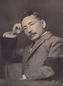 Sōseki Natsume: Um seine hysterische Cousine zu beschwichtigen, die mit ihm ausreißen möchte, reicht er ihr ein Exemplar von Natsumes satirischem Roman Ich der Kater (S. 51).