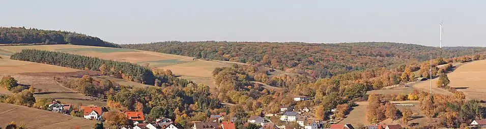 Blick über Hausen auf den westlichen Teil des Naturschutzgebietes Hausener Talhänge,der entlang des Hesselbacher Grundes verläuft (vor dem Wald mit Windrad)