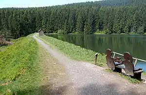 Damm und Wasserfläche des Neuen Grumbacher Teiches mit einer Bank des Liebesbankweges