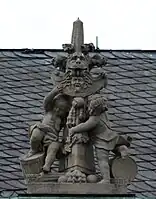 52. Trophäe –  Fiale, 2 Putten, Löwenkopf, Löwenpranke, Peltaschild mit Gorgonenhaupt, Goldenes Vlies, Kugeln.