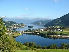 Foto einer um einen Fjord liegenden Ortschaft in bergiger Umgebung mit einem See im Vordergrund