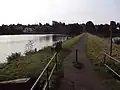 Blick über die Ausflutbrücke auf den Damm, die Wasserfläche und an die angrenzende Wohnbebauung.