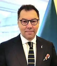 Porträt eines mittelalten Mannes mit Brille, dunklem Anzug und blaugelber Strickkrawatte vor ukrainischer Flagge