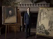 Georg Friedrich Prinz von Preußen posiert stehend und im Anzug zwischen zwei Gemälden.