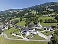Blick auf die Pfarrkirche zum Hl. Barholomäus, darunter das Gemeindeamt mit Volksschule und Kindergarten, im Hintergrund der Harter Berg