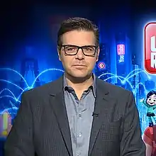 Ein junger Mann von vorne gesehen, sitzend, formell gekleidet und mit Brille.