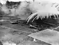Eine Phosphorbombe explodiert auf dem Flugfeld Lakunai. Zu sehen sind eine Mitsubishi G4M2 und eine Mitsubishi A6M3.