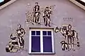 Historische Darstellung der Bewohner von Pilgers­dorf anno 1225. Gestaltet von F. Reidinger (1991) auf einer Hausfassade.