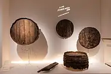 Verschiedene Fragmente von Holzfässern wie Böden, Deckel oder komplett erhaltene Fässer mit eingravierten Hinweisen wie Strichen für aufgeschriebene Schulden.