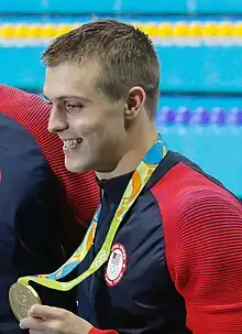 Ryan Held in blaurotem Trainingsanzug bei der Siegerehrung 2016, mit der rechten Hand zeigt er den Fotografen seine Goldmedaille.