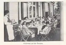 Schwarz-Weiß Bild von Kindern an einem Esstisch, darunter Schriftzug „Frühstück auf der Terrasse“