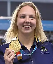 Sara Junevik mit dunkelblauer Trainingsjacke zeigt ihre Goldmedaille.