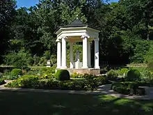 Heutige Ansicht des im Jahre 1803 errichteten Musentempels mit einer häufig fälschlich als Polyhymnia bezeichnete Kalliope-Skulptur im Zentrum sowie aufwendiger Schmuckbepflanzung rund um die Parkarchitektur herum.