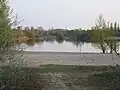 See Binsfeld, Blick von Nord nach Süd auf den schmalen Durchstich zum See Kuhunter und dessen Südufer. Dahinter ist der Rastplatz Binshof der A61 zu erkennen. Der Bohrturm der Erdölbohrung Römerberg 2, liegt schon hinter der Autobahn im Süden. Ganz im Hintergrund der Speyerer Müllberg.