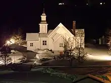 Foto einer in der Dunkelheit beleuchteten, weiß gestrichenen Holzkirche
