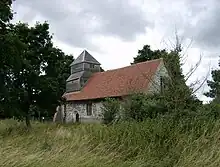 Eine Kirche aus Feuerstein mit rotem Ziegeldach und einem verschindelten Kirchturm am fernen Ende