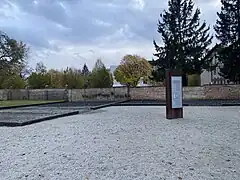 Das Fundament der ehemaligen Anstaltsscheune, im Hintergrund eine Mauer und Bäume.