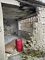 Zerstörter Eingang mit der Tür auf dem Boden. Das Ölfass war nicht Teil der Ausstattung.