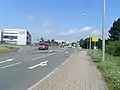 Die Kreuzung Auer Stra­ße / Zwic­kauer Stra­ße in Stoll­berg Rich­tung Nor­den ge­se­hen. Hier soll ein Kreis­ver­kehr ent­ste­hen, an dem die Bahn­stre­cke von Stra­ßen­mit­tel­la­ge (im Bild­hin­ter­grund) in Sei­ten­la­ge (Wiese im Bild rechts) we­chseln wird.