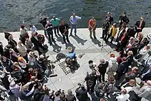 Blick von oben auf die Verlegung, eine Menschenmenge bildet einen Kreis um den Künstler, der am Boden vor den Steinen kniet.