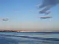 Wolken und Mond über dem Meer, am Horizont eine Küstenlinie