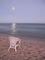 Weißer Stuhl an einem Strand, der Mond spiegelt sich im Meer