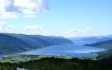 Foto eines Fjords in bergiger Umgebung. Am inneren Ende des Fjords befinden sich einige Gebäude