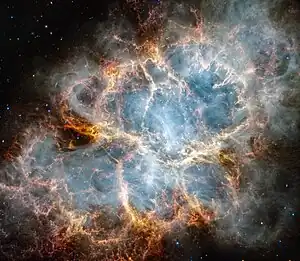Infrarotaufnahme des Krebsnebels mithilfe des James-Webb-Weltraumteleskops: Die Struktur des Pulsarwind-Nebels ist bläulich-weißlich erkennbar, die der Filamente und der Staubverteilung orange-rot.